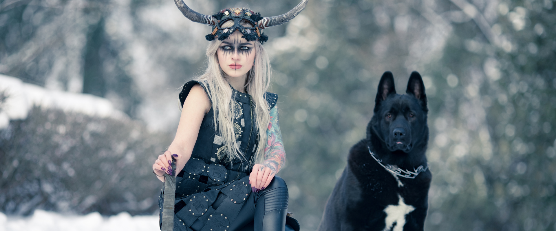 woman dressed as a viking next to a black and white dog in a snowy forest