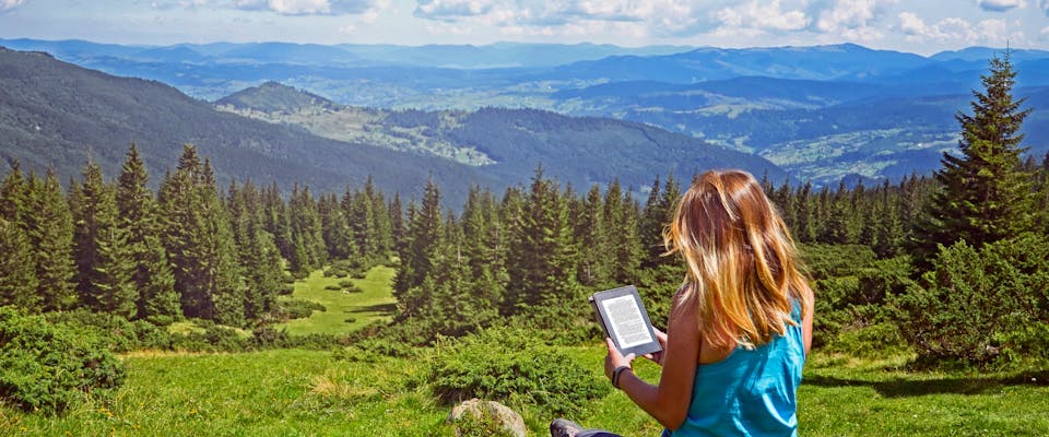 A woman reading an e-book in the mountains.