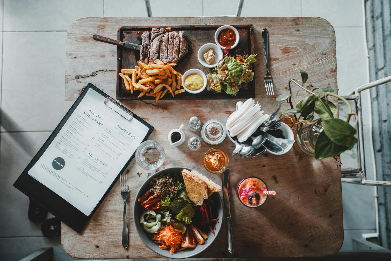 Restaurant table setting with an open menu beside a plate of steak and fries.