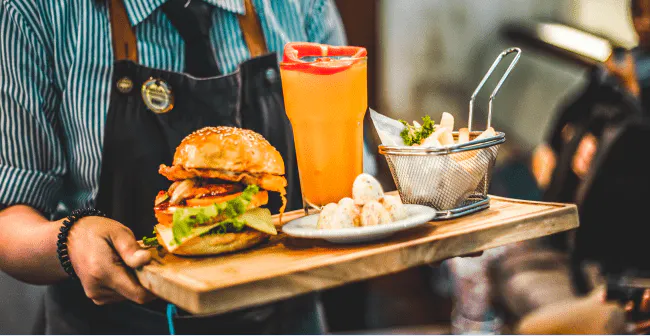 Image of a restaurant worker dropping off food and drinks to a customer