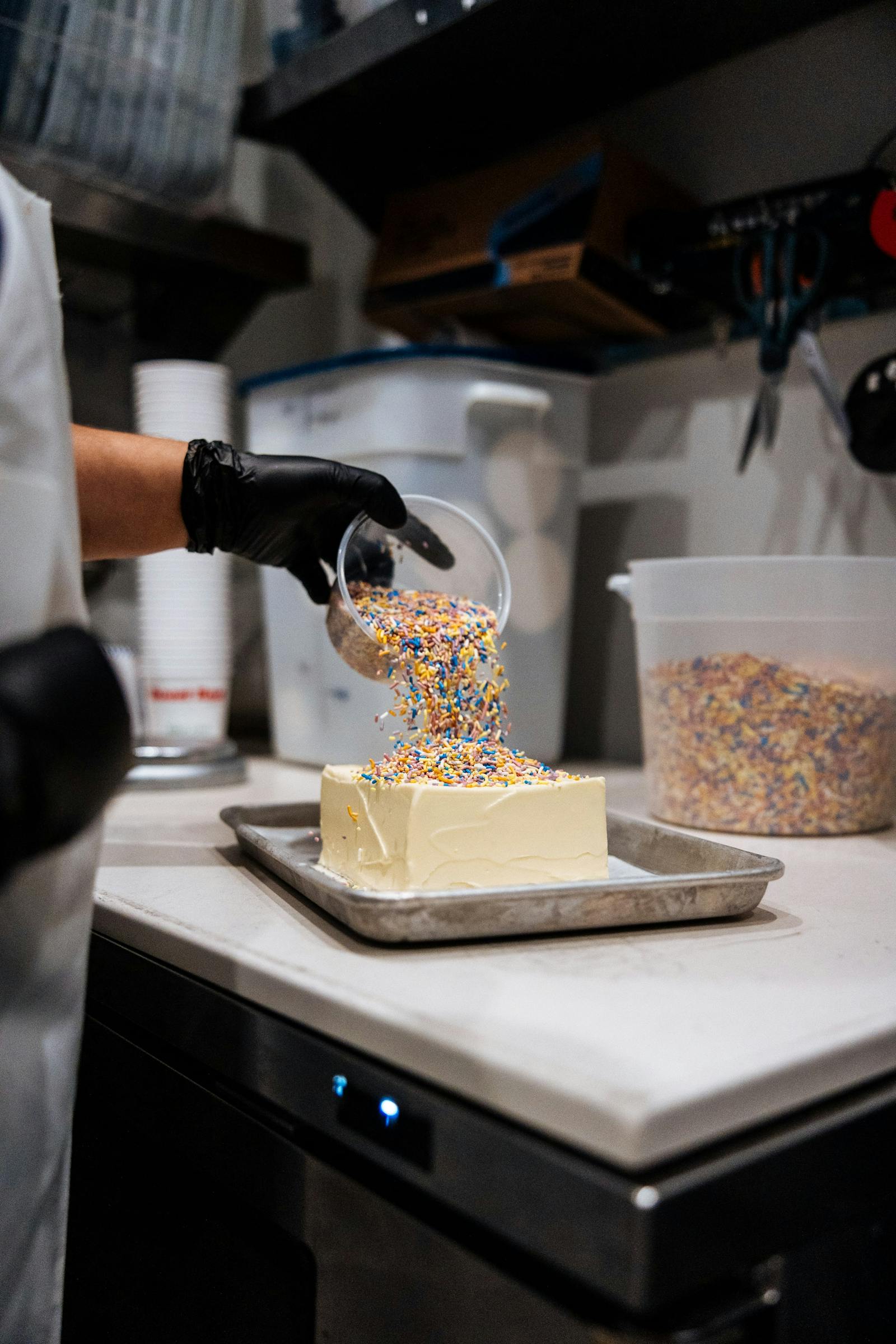 A chef pouring sprinkles on a cake. 