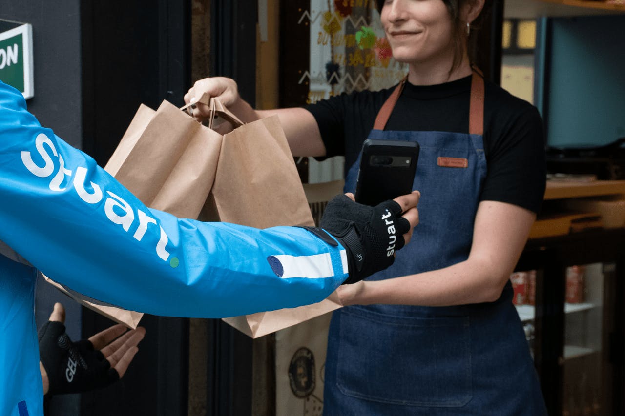 Image of a restaurant staff passing food delivery bags to a Stuart delivery rider