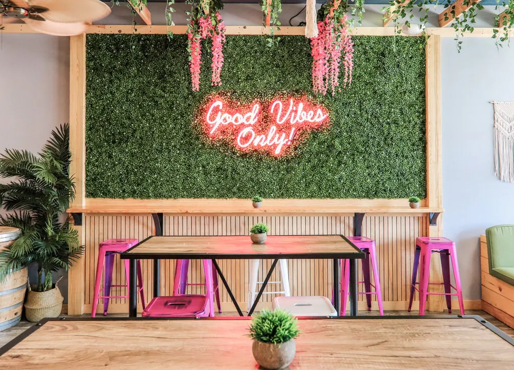 Image of a plant wall with pink neon sign that says "Good vibes only!" in the Sweetberry dining room