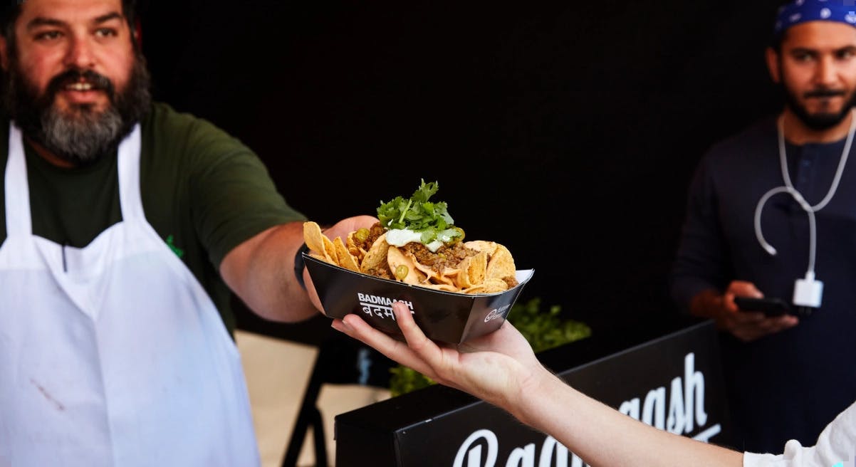 Image of a cook handing a paper box of nachos to a customer