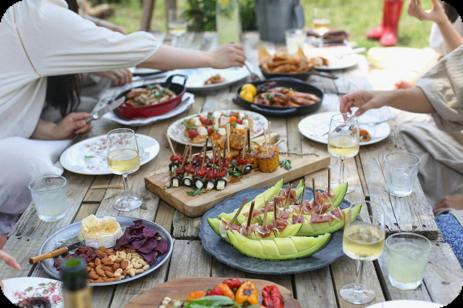 Image of a group dining at an outdoor table with summery food and wine