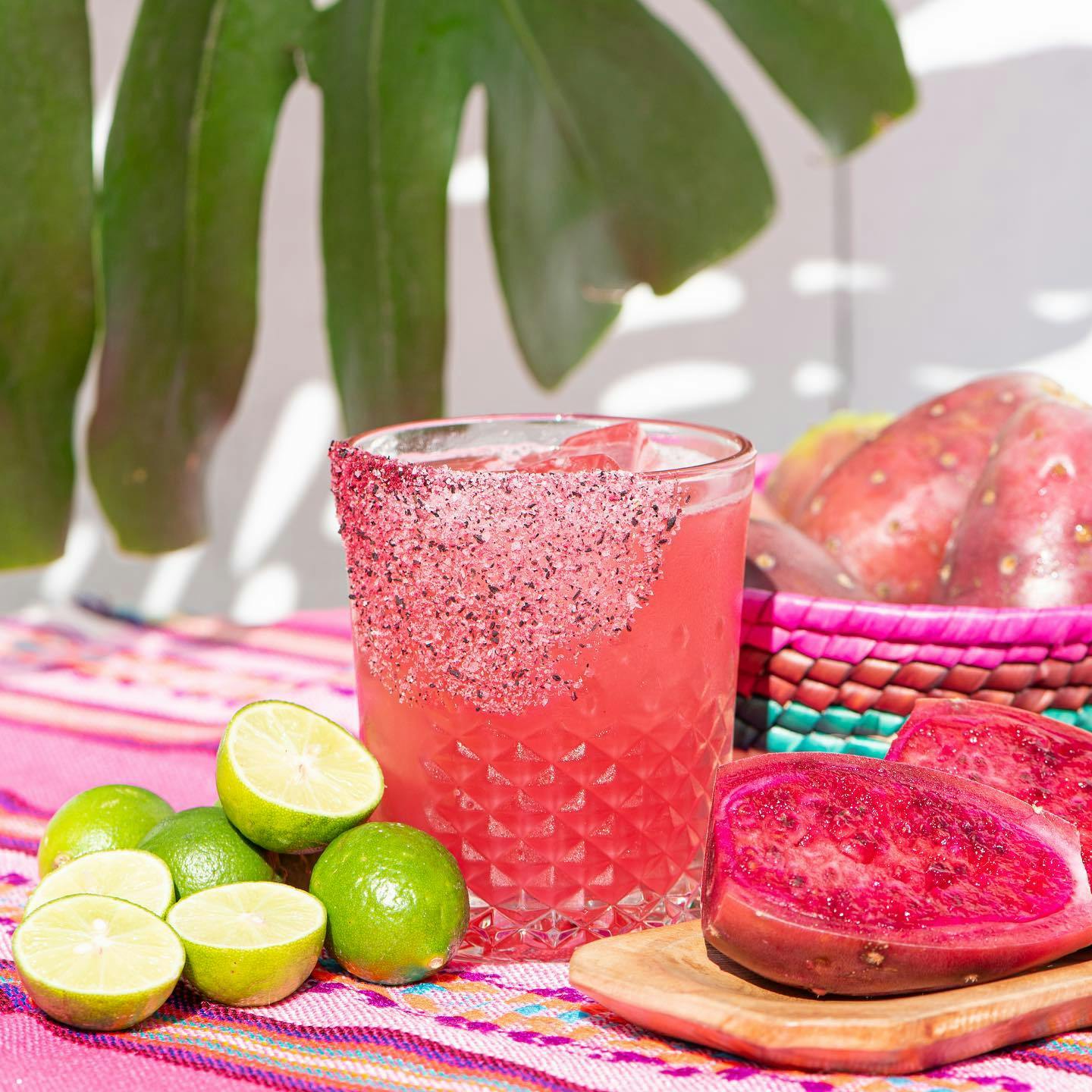 Image of a bright pink Margarita in a salted glass surrounded with limes and passionfruit
