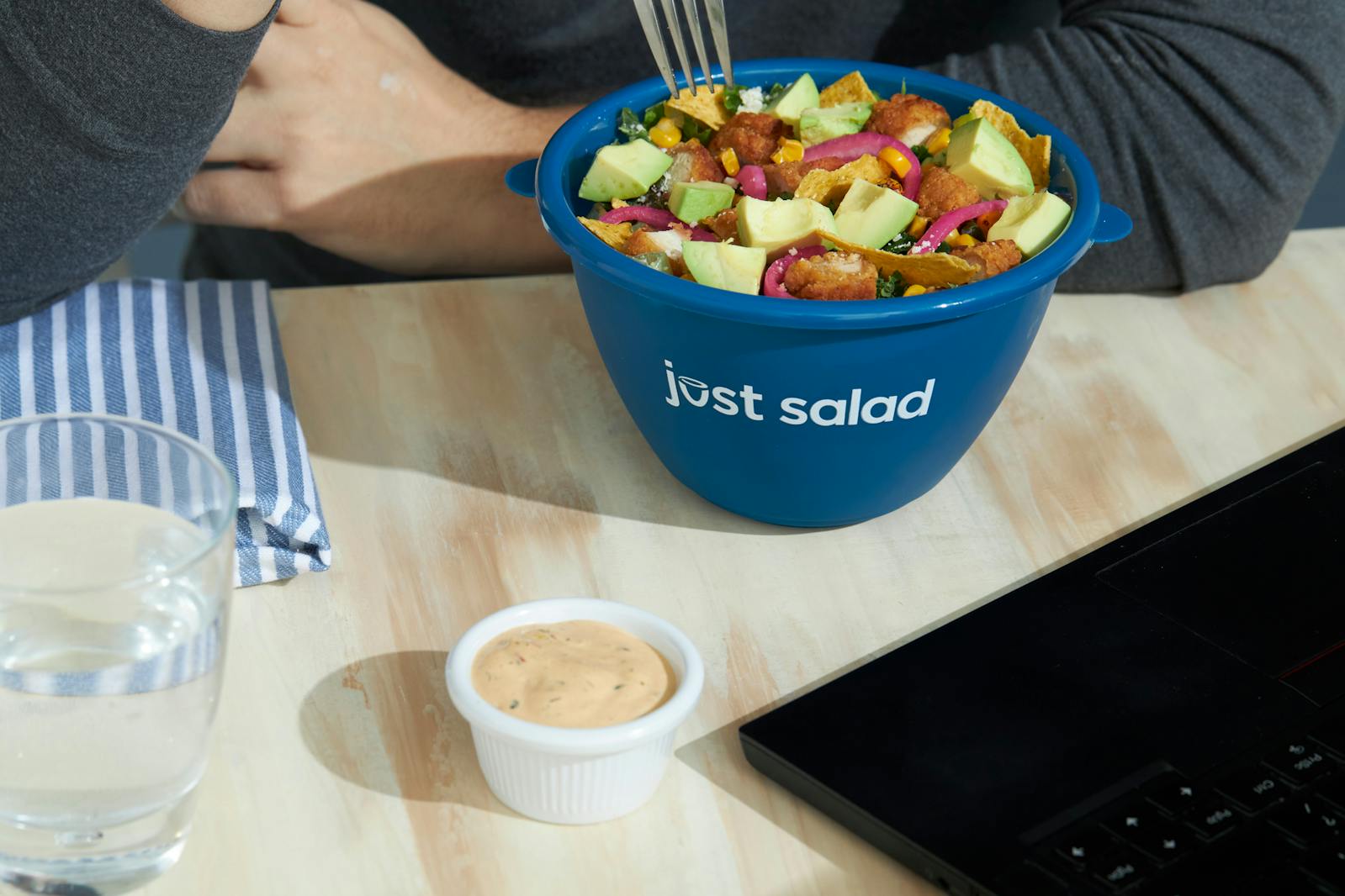 Image of Just Salad bowl sitting on a table next to a side of dressing and a glass of water