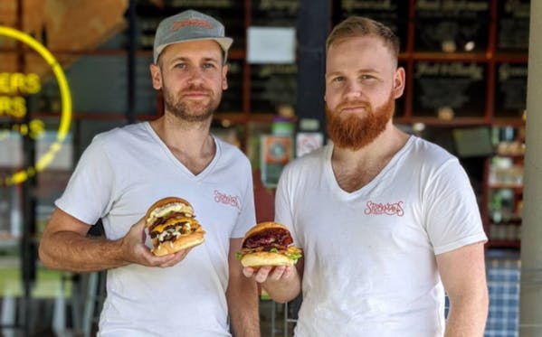 Image of two restaurant owners in Stockmans t-shirts holding burgers in their hands