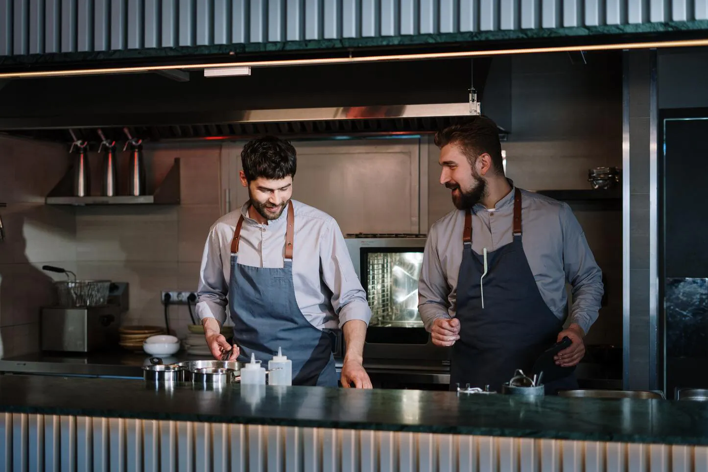 Image of two restaurant workers in aprons prepping behind the open kitchen