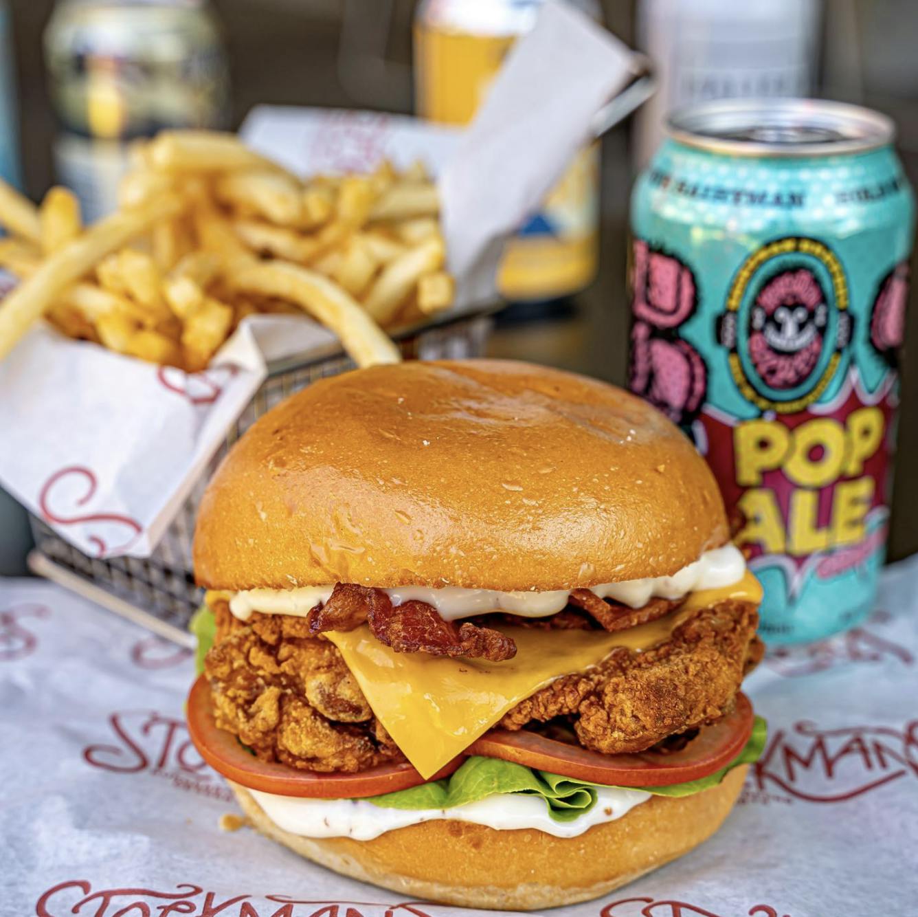 Image of a fried chicken burger with a can of craft beer and French fries in the background