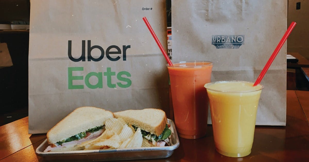 Image of Uber Eats bag with a sandwich, chips, and two juices in front of it