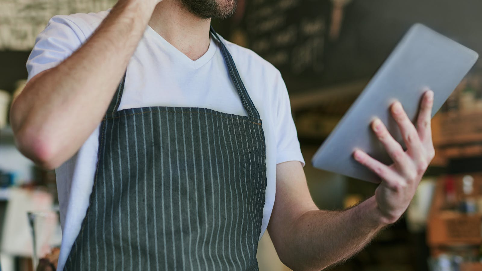 Image of a restaurant employee talking to a customer on the phone while looking at his tablet