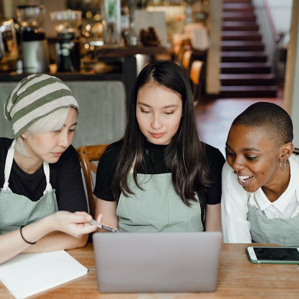 Image of three women working at a restaurant, looking at their sales on a computer.