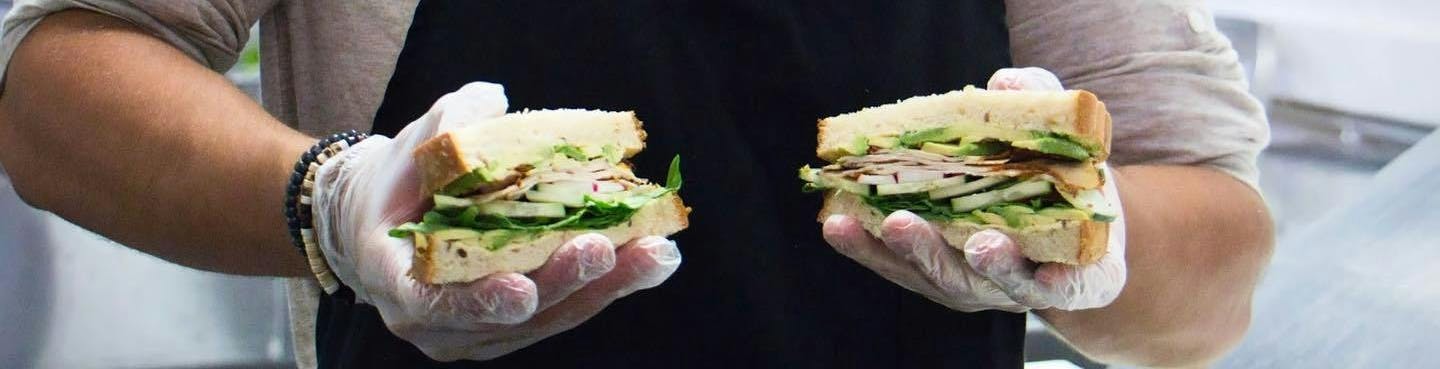 Image of Urbano Food Group employee holding up two sandwiches.