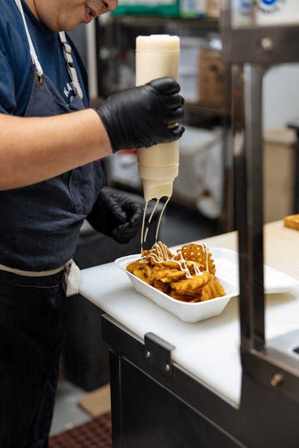 Image of a restaurant employee topping a delivery order of waffle fries with sauce