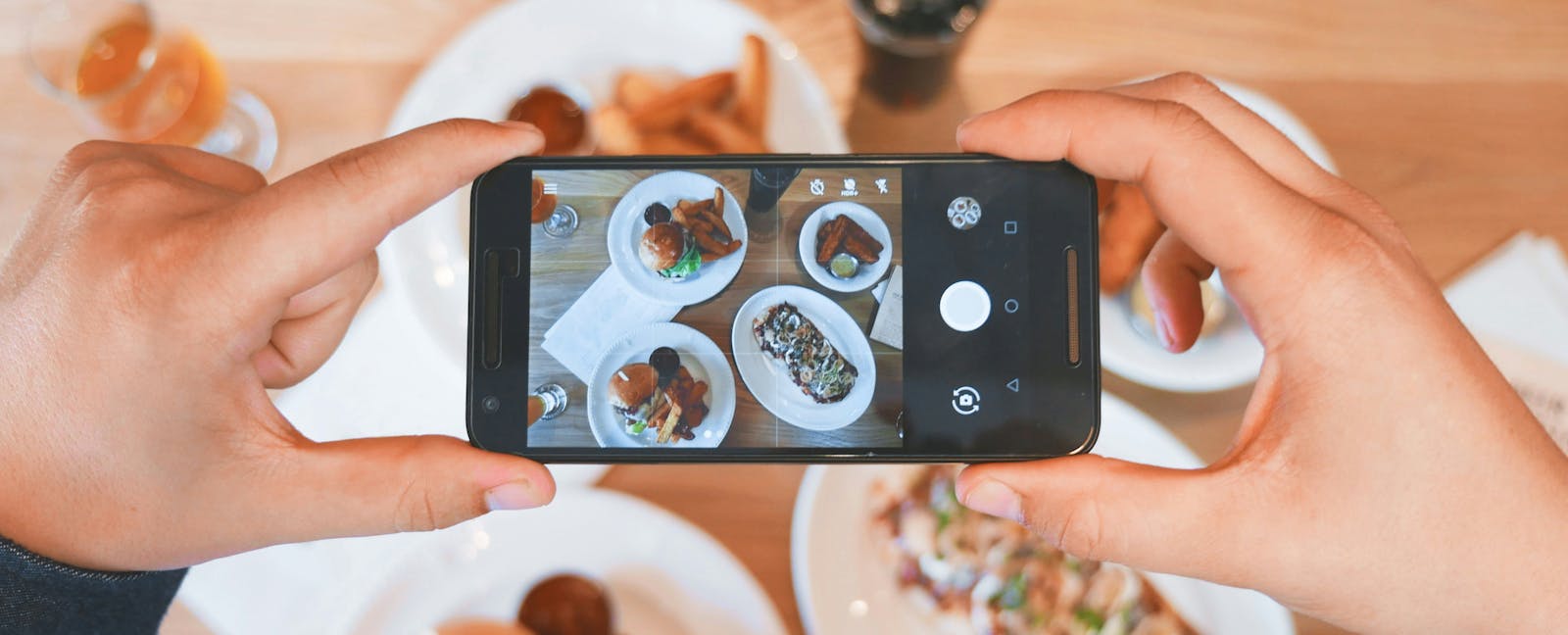 A foodie taking a picture of several dishes at a restaurant for Instagram.