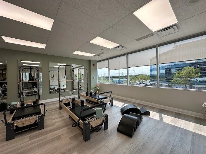 Sunlit reformer zone with neatly arranged Pilates machines, light wood accents, and an airy, organized layout.