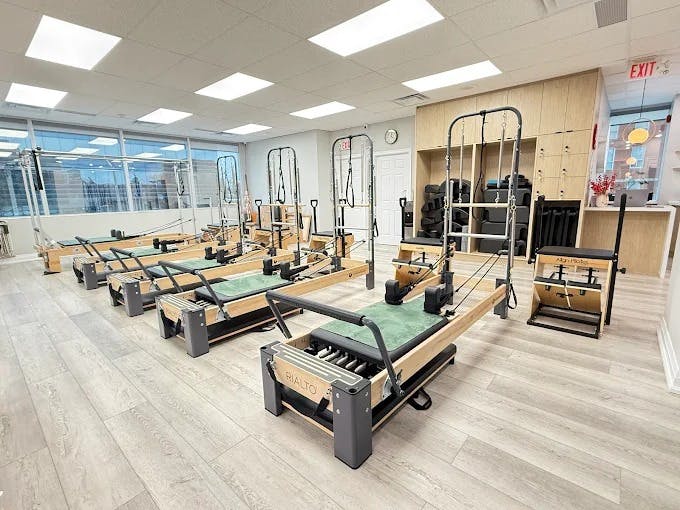 Wide view of the Pilates equipment area showing orderly machine placement, bright windows, and a serene, spotless environment.