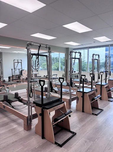 Minimalist Pilates zone featuring towers and chairs, bathed in soft sunlight with clean flooring and a tidy, open layout.
