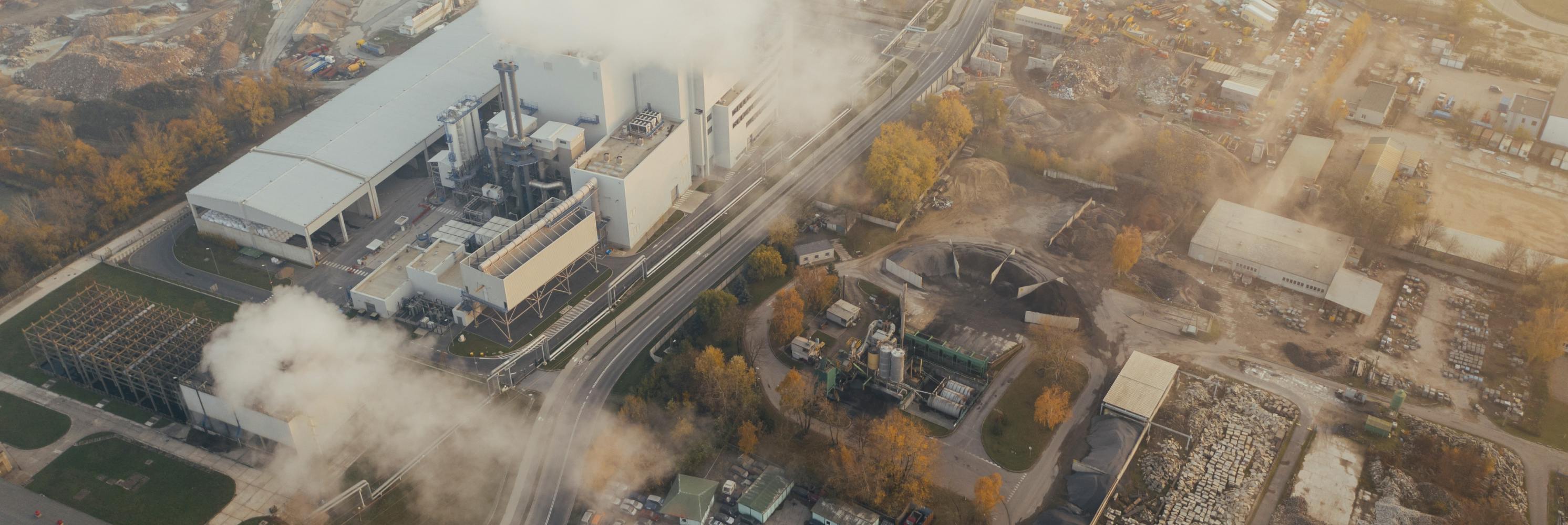 Aerial view of an industrial site emitting steam or smoke, surrounded by infrastructure and vegetation.