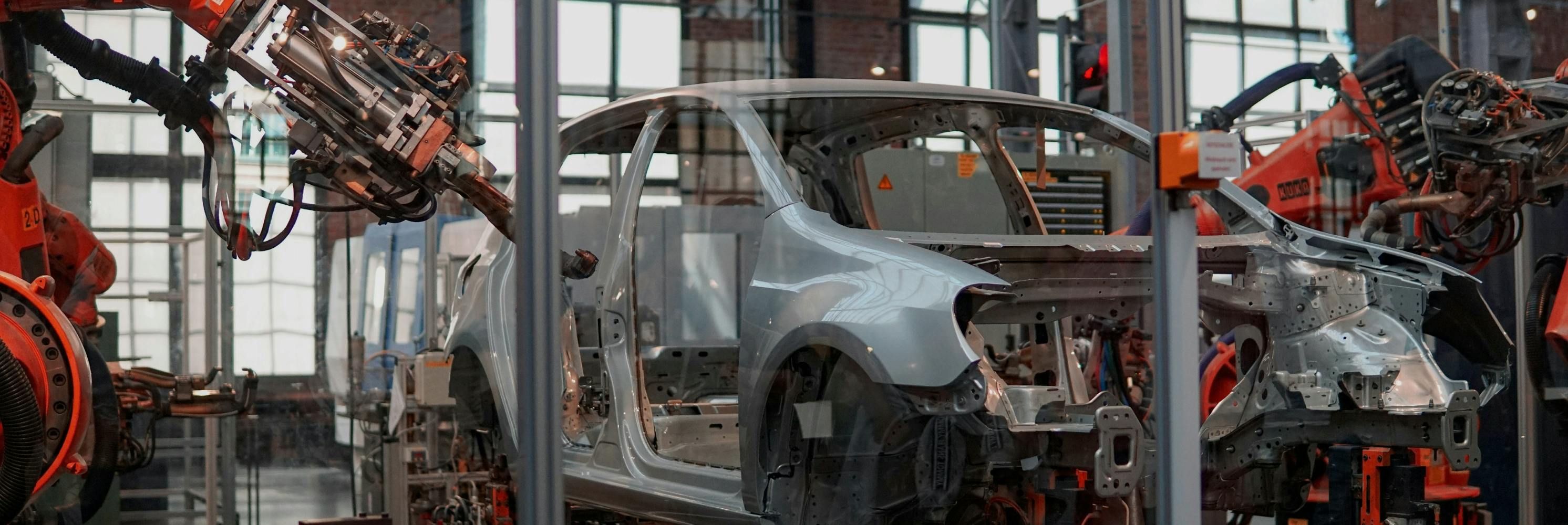 Automated car manufacturing line with robotic arms assembling vehicle frames in a factory.