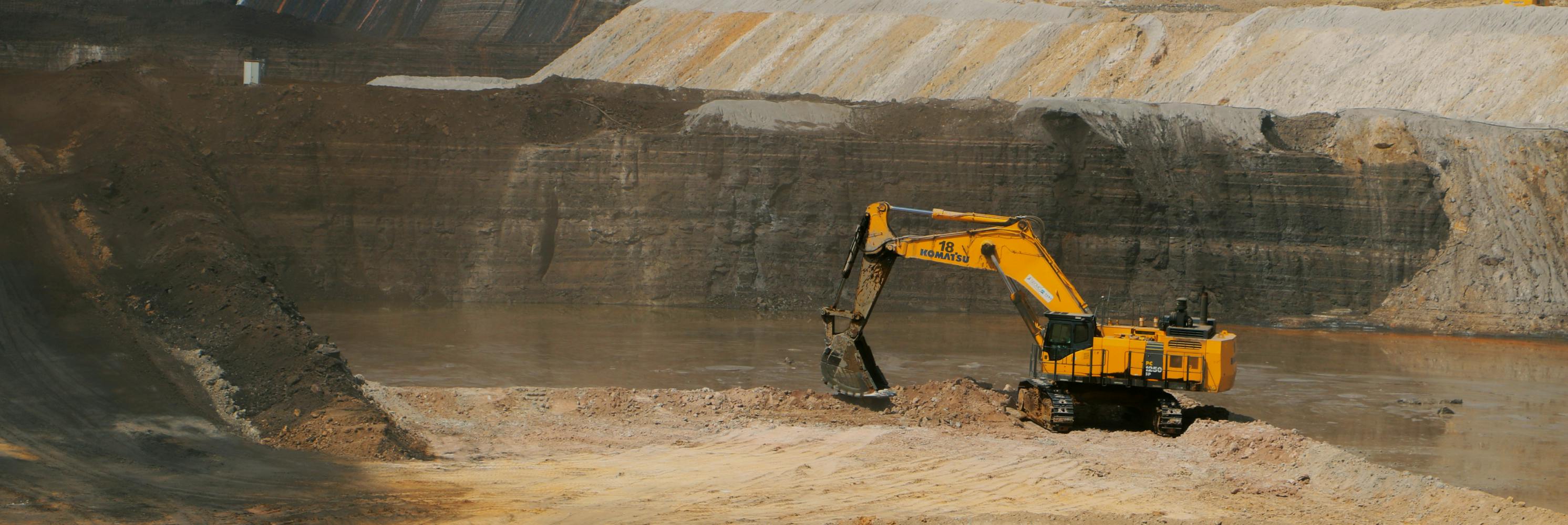 Wide-angle photo of an open-pit rare earth mine with a large Komatsu excavator operating in the pit, showcasing the scale of mining operations involved in extracting rare earth minerals.