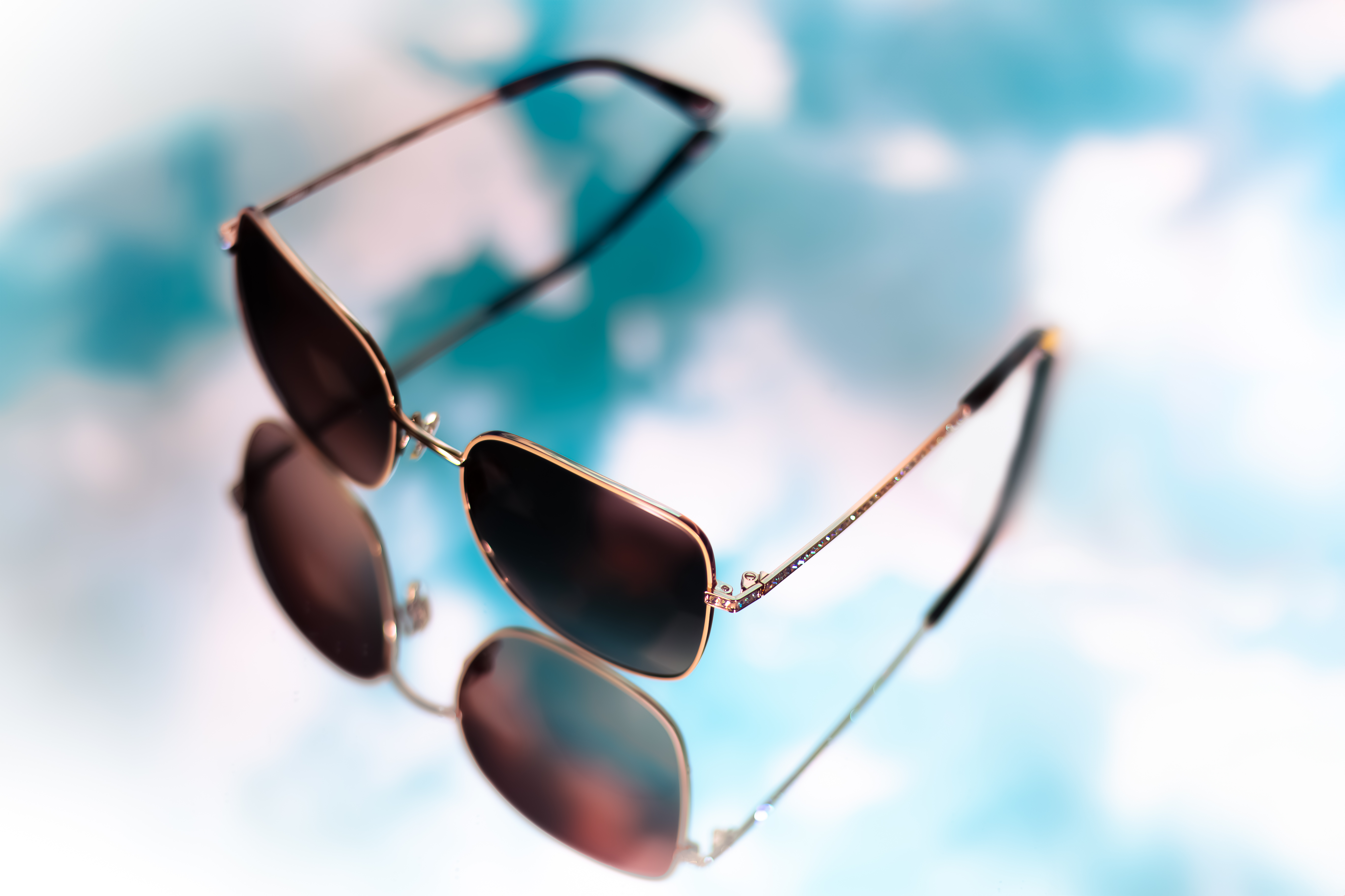 Product photography of Jimmy Crystal sunglasses on a mirrored background against a blue sky