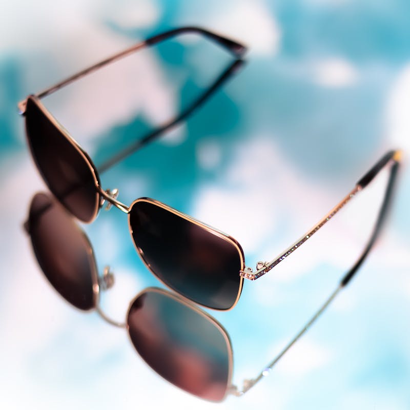 Product photography of Jimmy Crystal sunglasses on a mirrored background against a blue sky