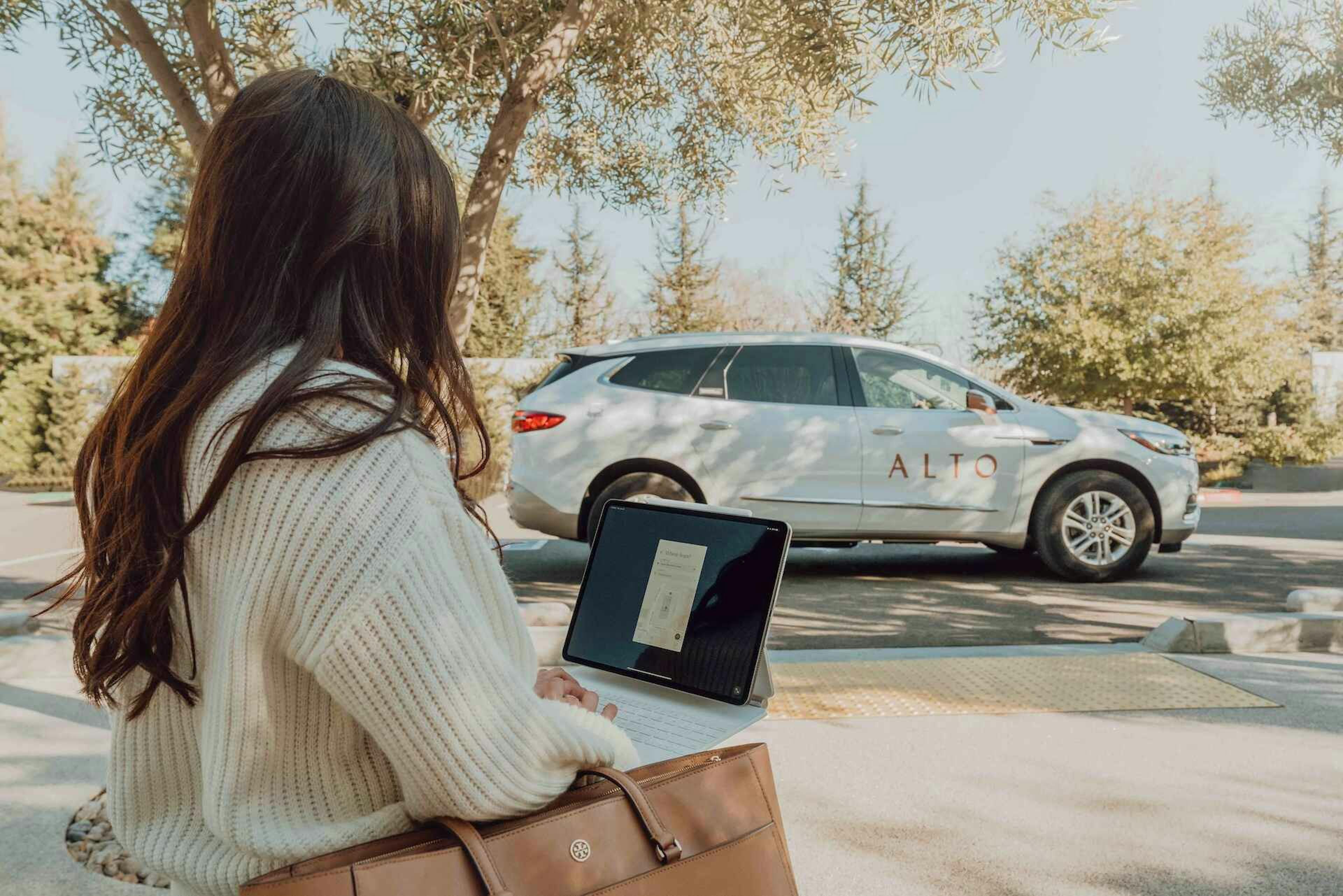 Alto rideshare car sits in the street while woman books a car ride on her computer