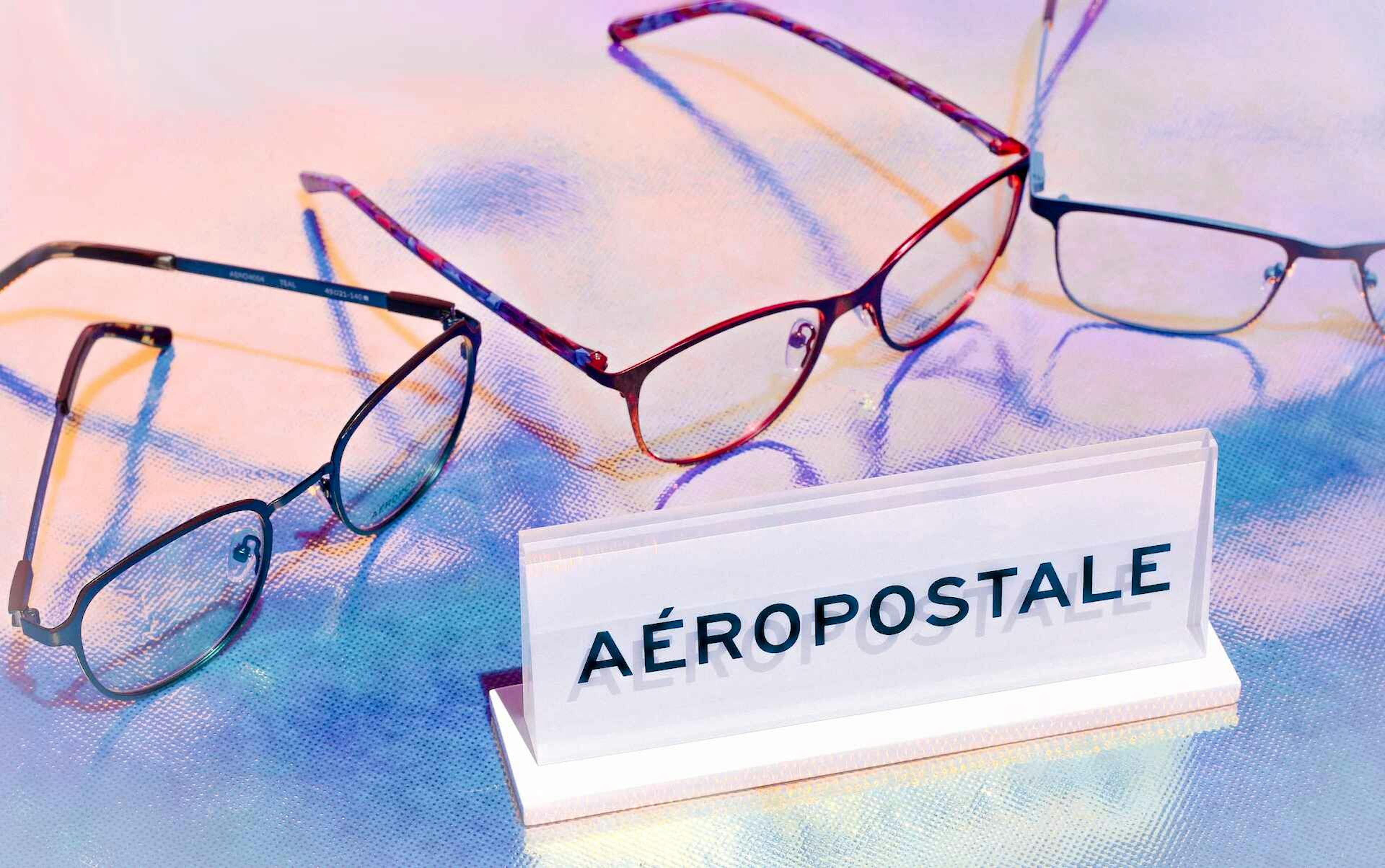 Three colorful Aéropostale eyeglass frames on an iridescent background with the Aéropostale placque