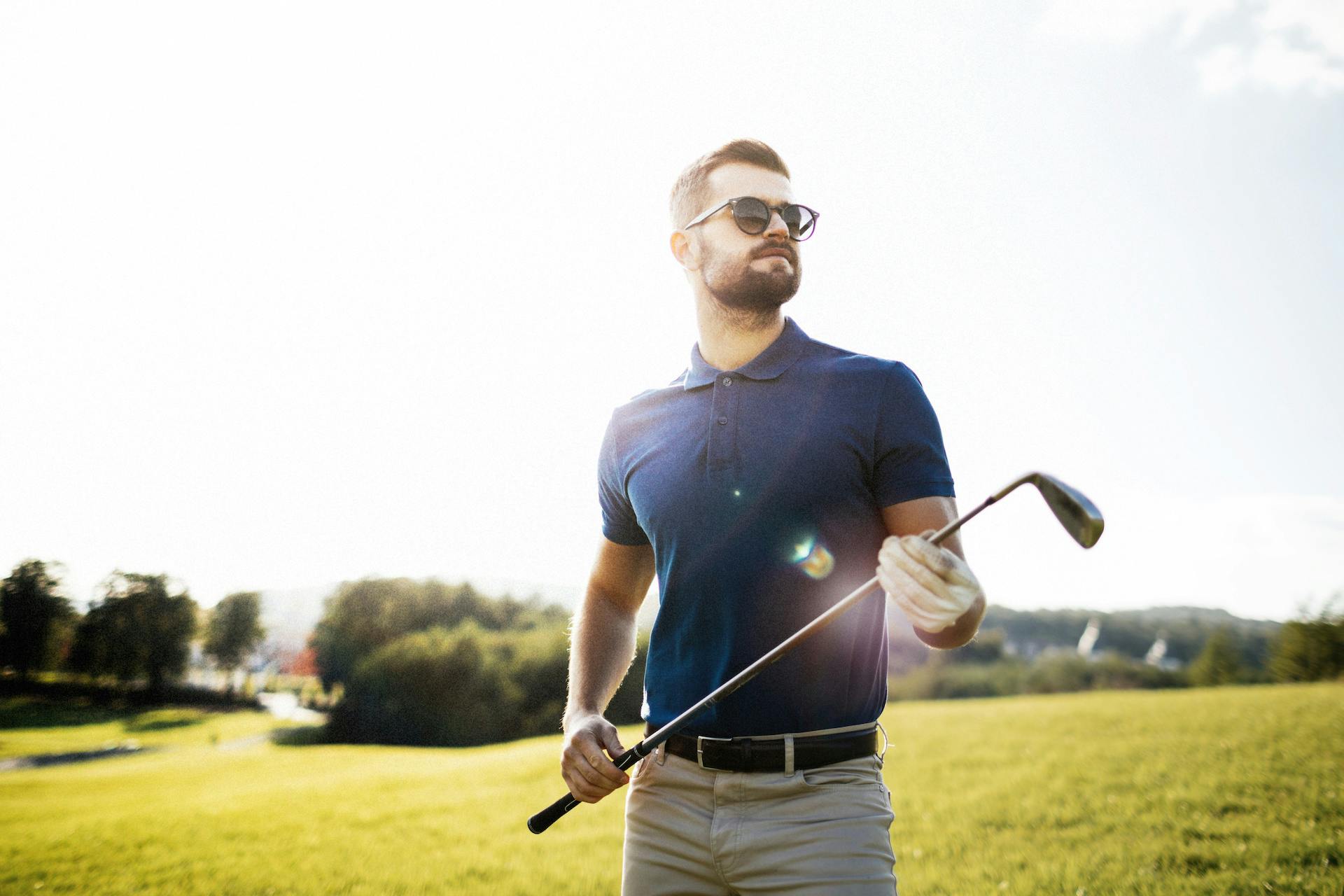 Young man in sunglasses standing on a golf course holding a golf club