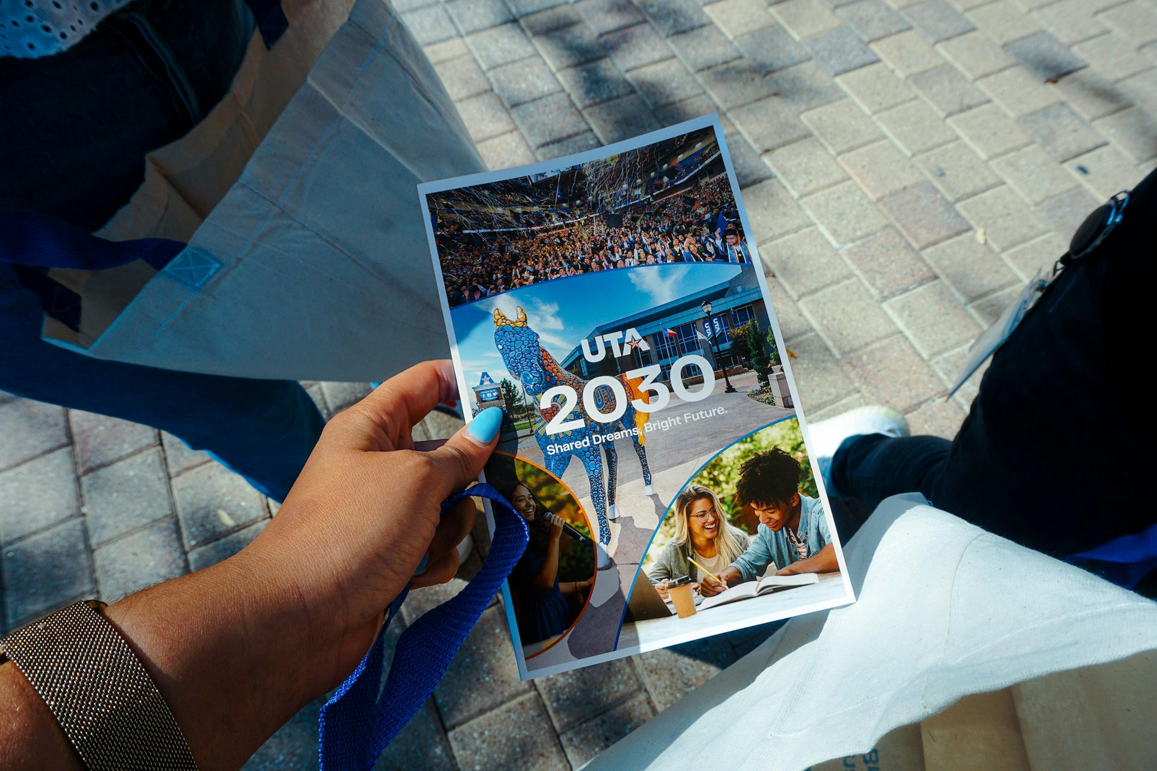 A hand holding a "UTA 2030" brochure with images of students and campus life.