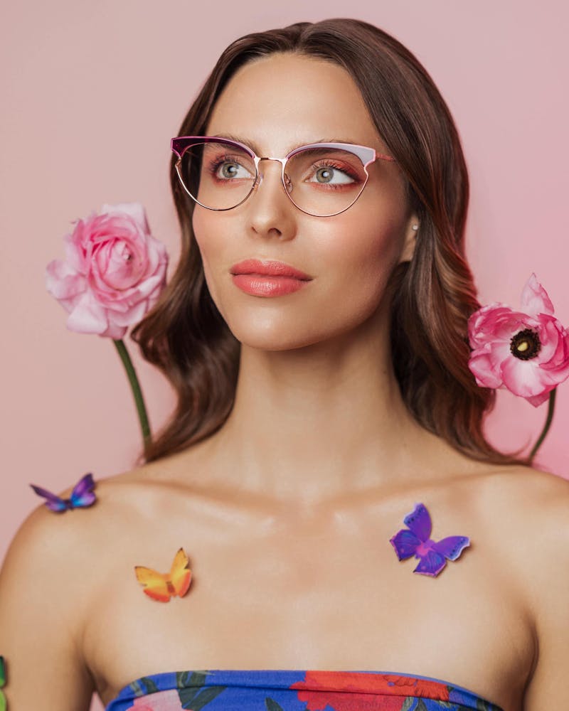 A woman modeling a pair of RACHEL Rachel Roy glasses, wearing a floral outfit on pink background.