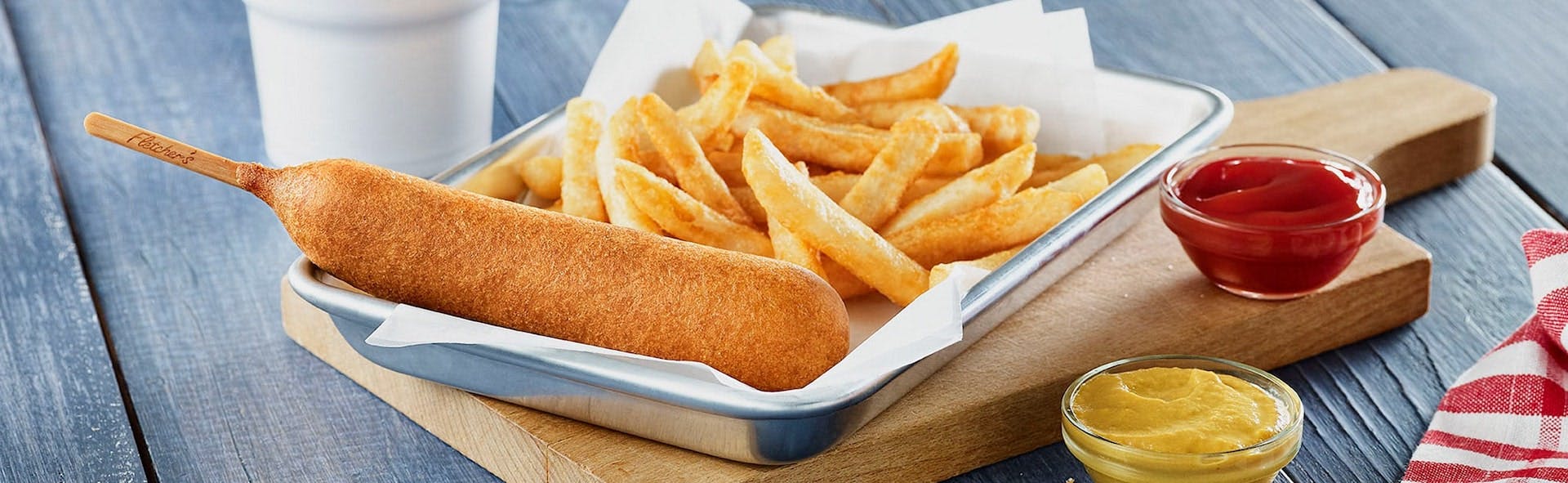 Golden chicken corn dog from fletchers with a basket of fries beside ketchup and mustard