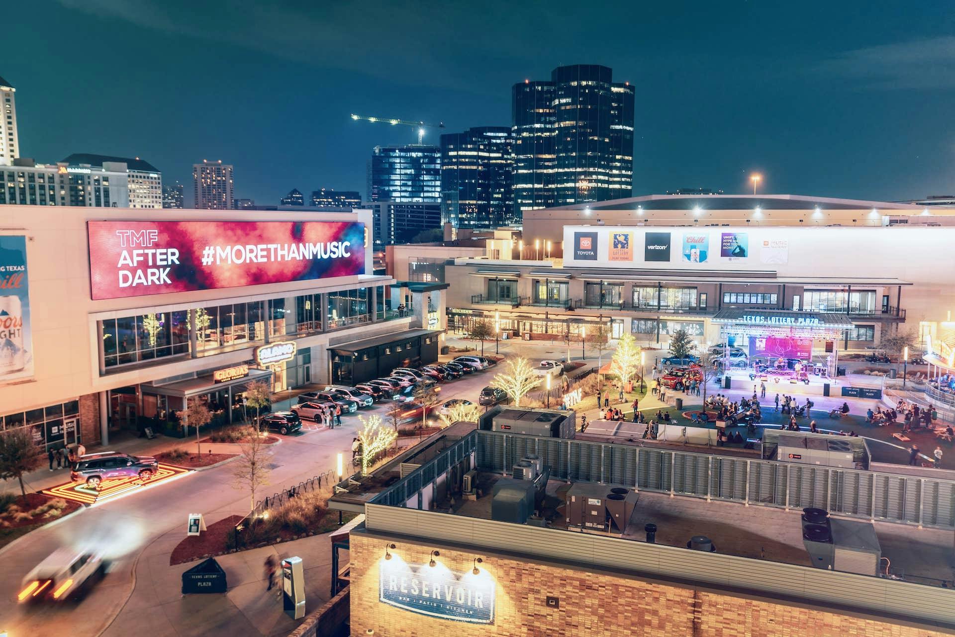 Evening view of the Toyota Music Factory with illuminated signs, bustling with people and activity.