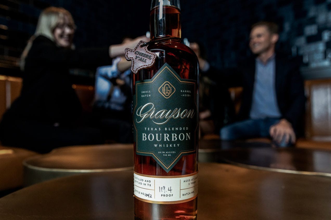 Grayson Whiskey bottle with two people smiling and cheering in the background