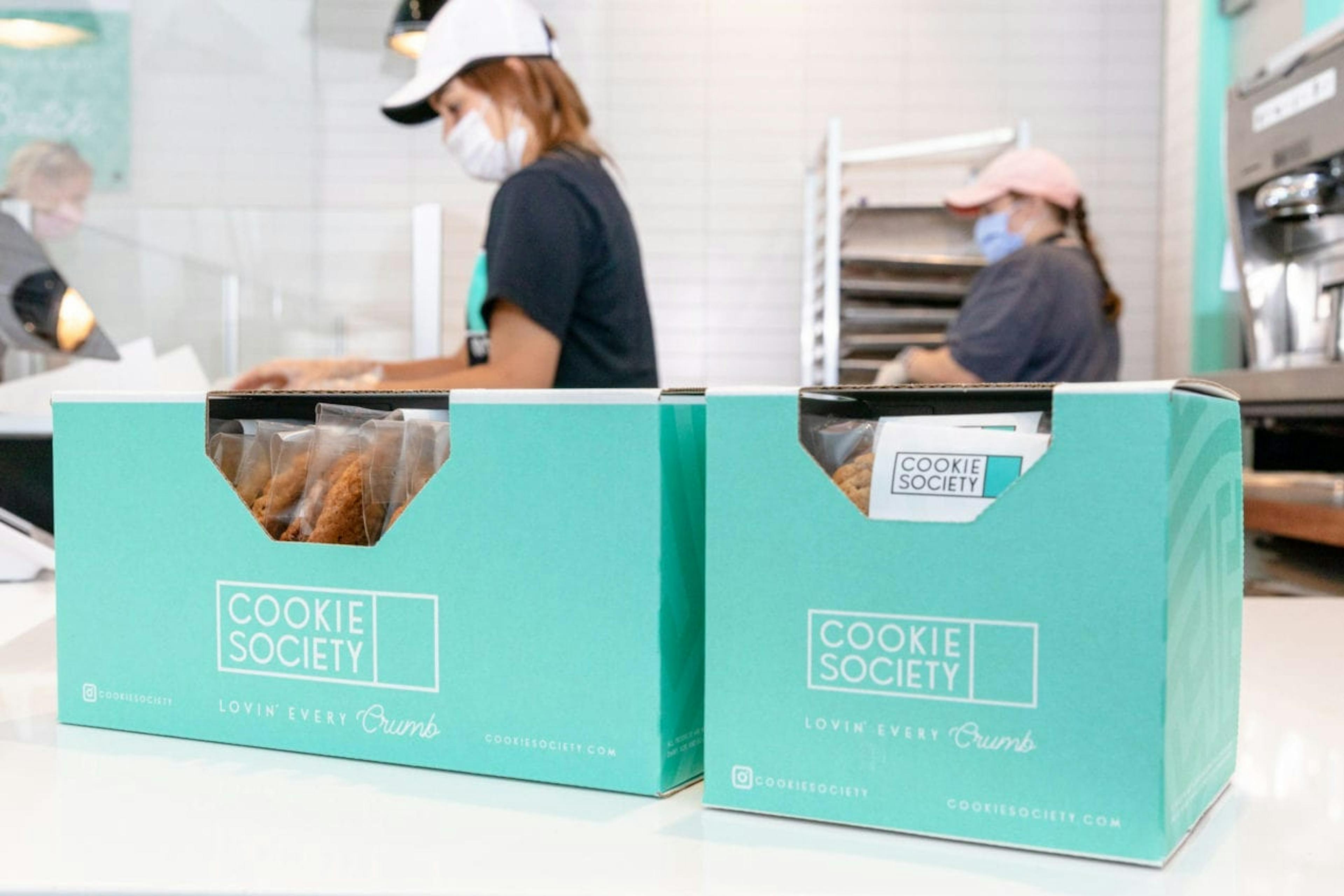 Cookie Society cookies in boxes with employees working in the background