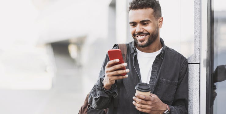 homem olhando o celular e segurando um copo de café