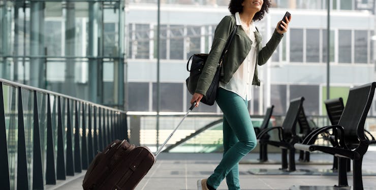 mulher no aeroporto olhando para o celular e carregando sua mala