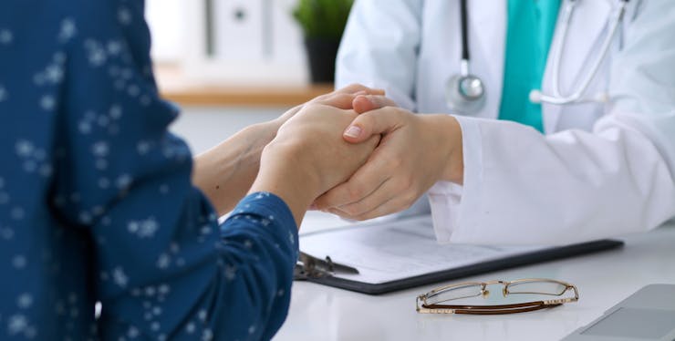 Paciente segurando a mão de médica no consultório