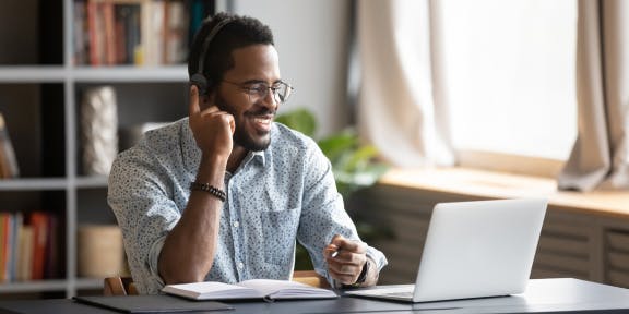 Homem falando pelo notebook com uma agenda a sua frente.
