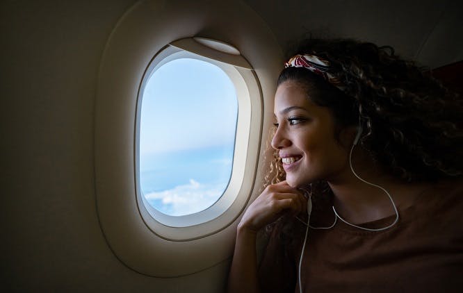 mulher viajando de avião e escutando música em seus fones de ouvindo enquanto olha pela janela e sorri