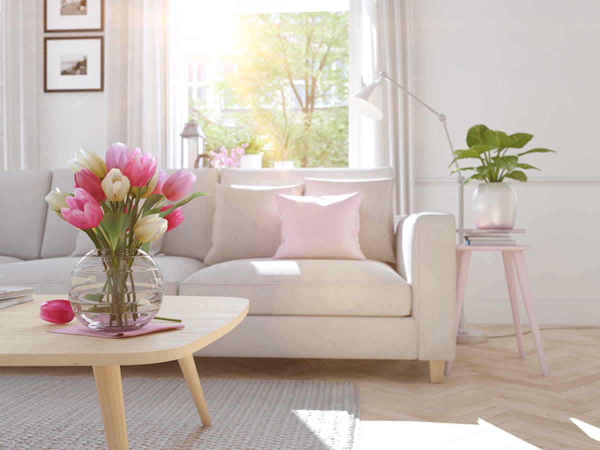 A clean living room with a white couch in front of a window and a coffee table with pink flowers