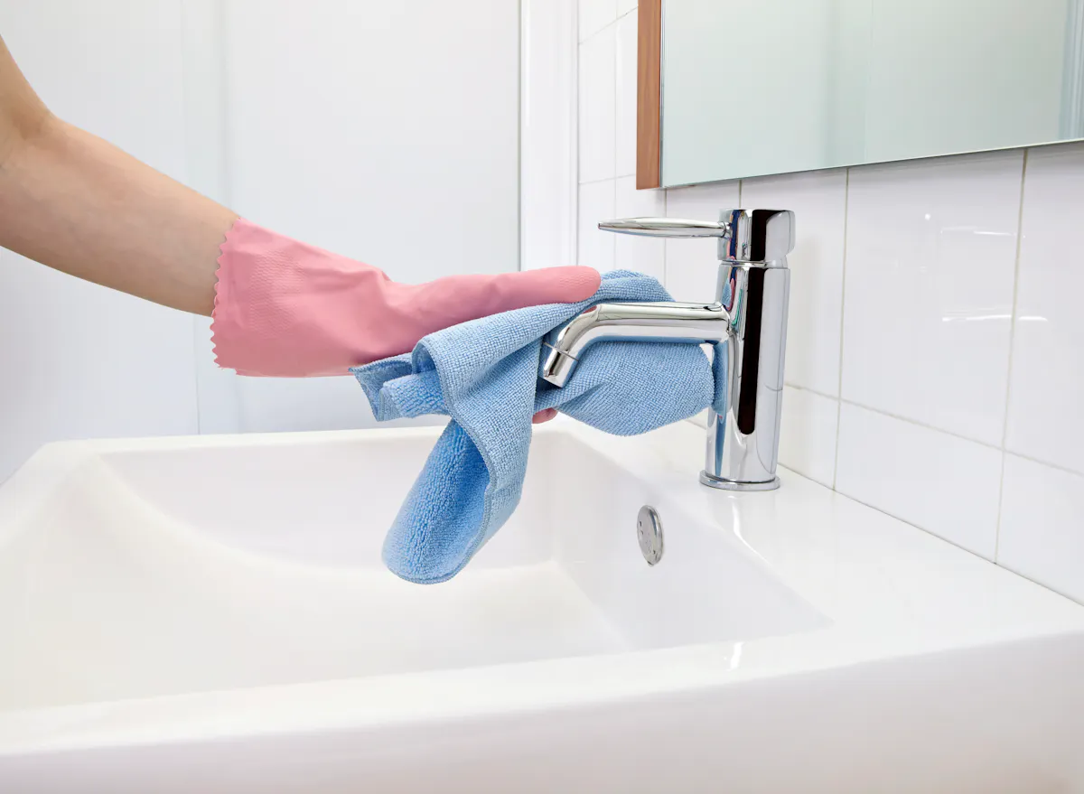 person with glove on cleaning bathroom sink