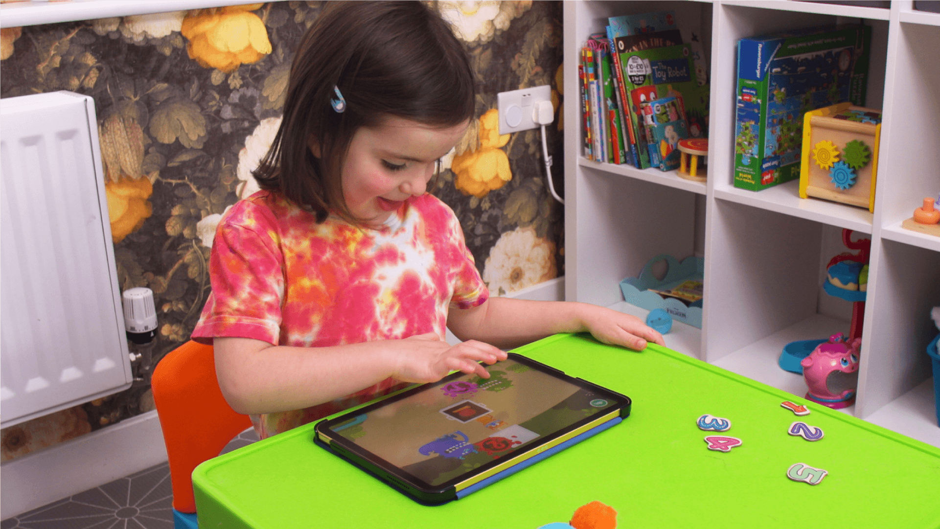 A happy young girl plays Teach Your Monster Number Skills on a tablet.