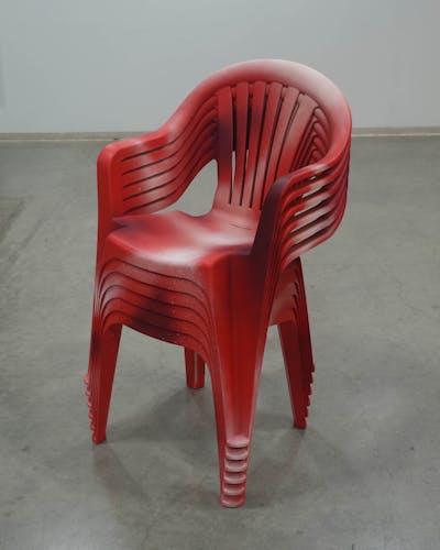 A stack of six plastic lawn chairs spray-painted with varying shades of red and white to imitate the texture of raw beef.