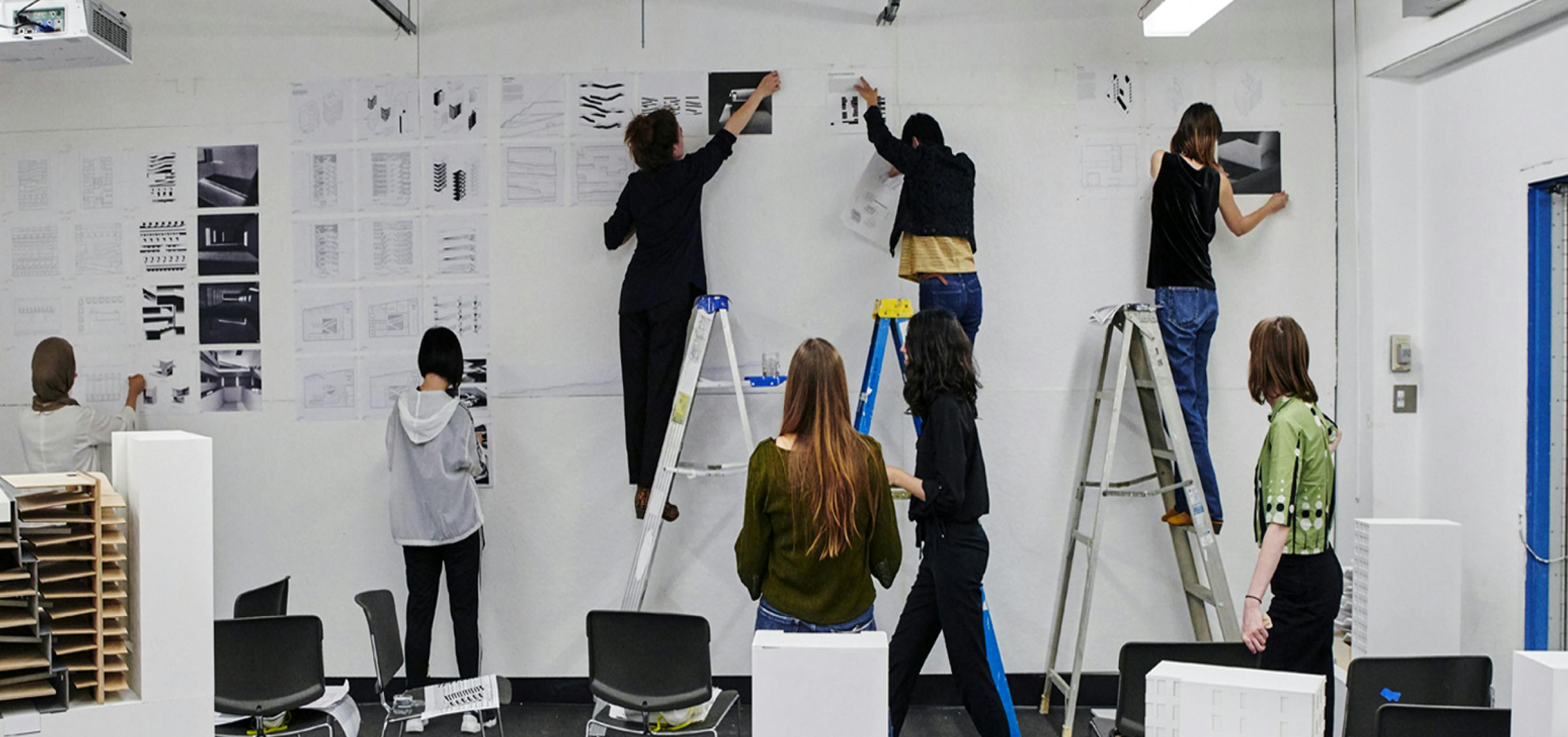 students on ladders hanging prints on a white wall