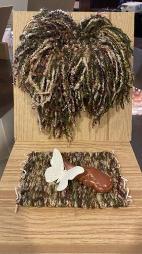 Woven wall piece and mat (green, brown, tan, hints of purple), white clay butterfly and red clay catfish laying together on mat