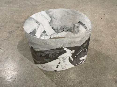 Graphite drawing on cloudy transparent paper sits on the floor forming a loop. Drawing includes figures and city landscape.