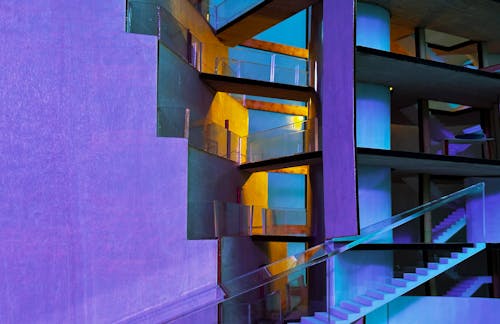 Architectural model of large building with bridged pathways across terraced crevasse. Purple, blue, and yellow lighting. Materials: acrylic, plywood, white PLA filament.